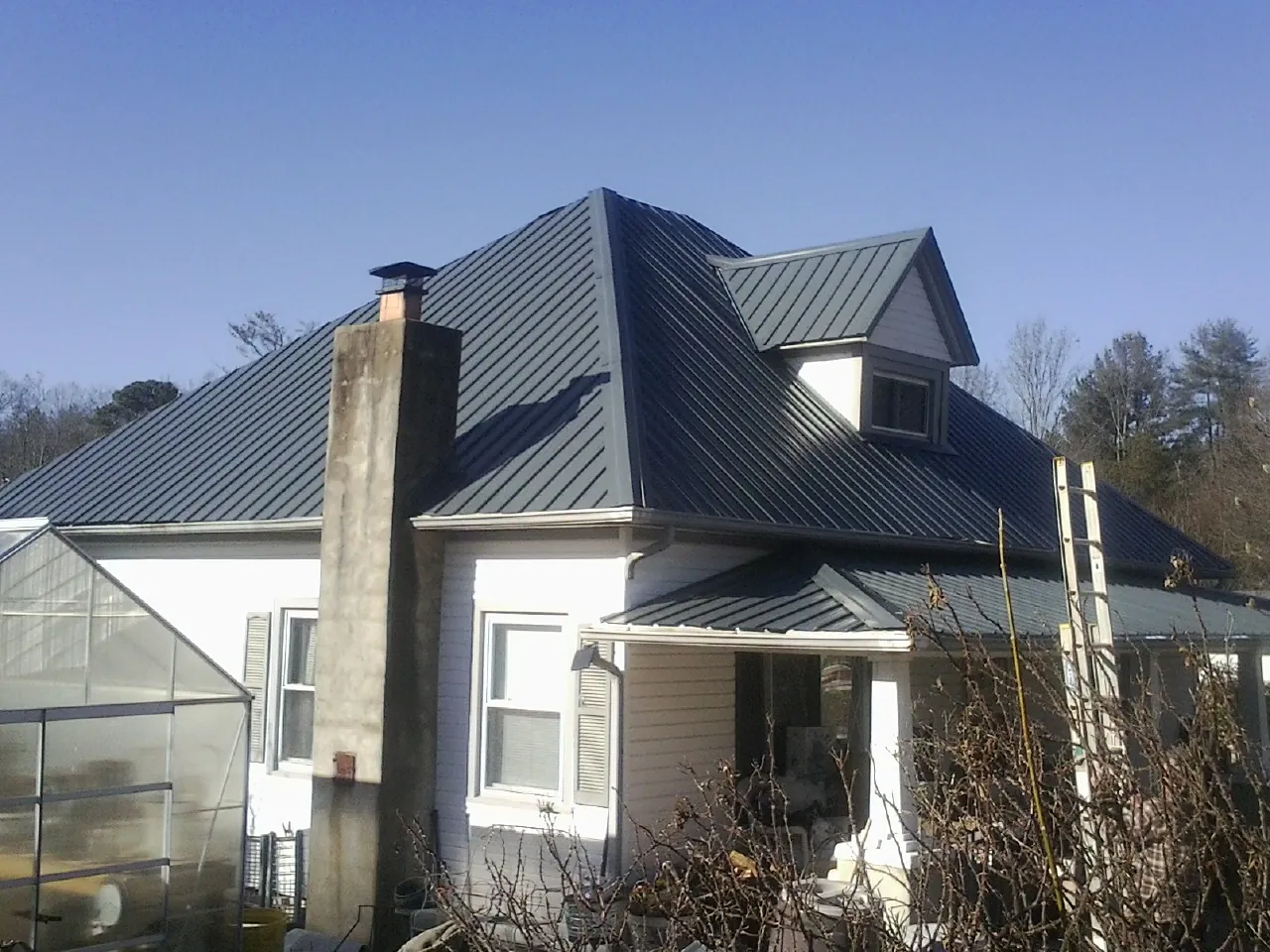 Dark blue standing seam metal roof on a white farmhouse with dormer — Slate & Tile Roof Repair by Roofing Brothers in Little Falls