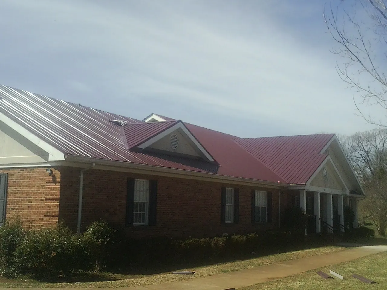 Red metal roof with gabled entries on a long brick building, from a Hail Damage Roof Repair job in Little Falls