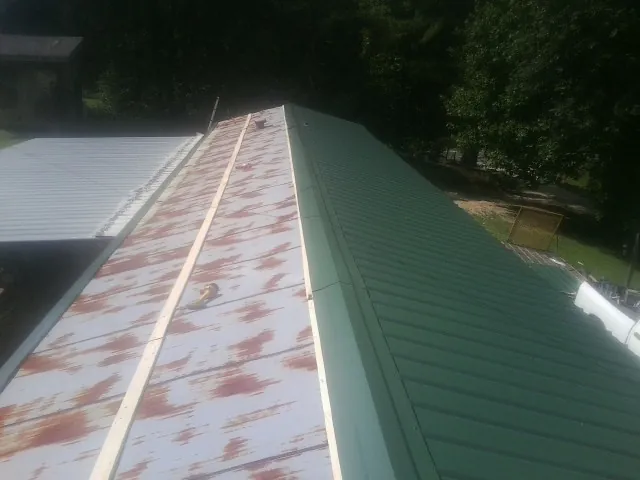 Old rusted panels beside newly installed green metal roofing — Wind Damage Roof Repair by Roofing Brothers in Little Falls