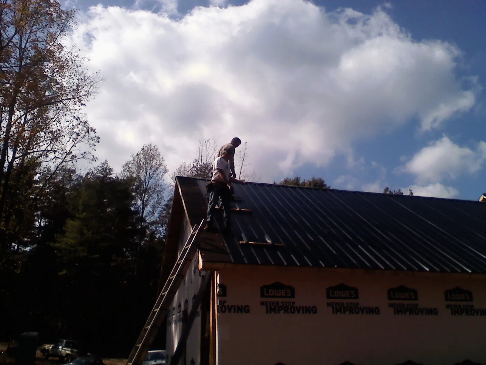 Roofer fastening dark metal panels high against a cloudy sky, from a Roof Inspection job in Little Falls