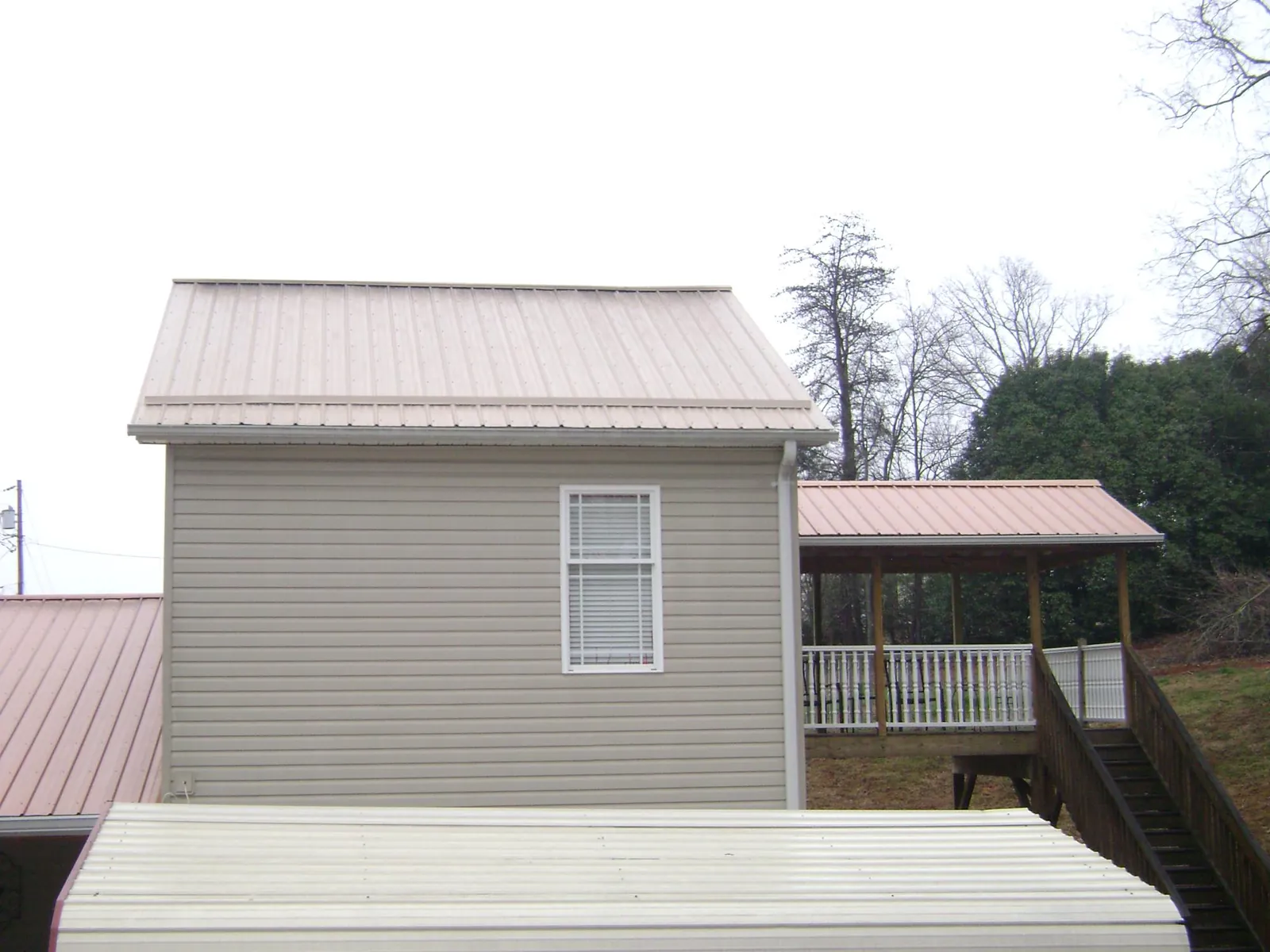 Tan metal roofs on a two story addition and attached porch, from a Roof Replacement job in Little Falls